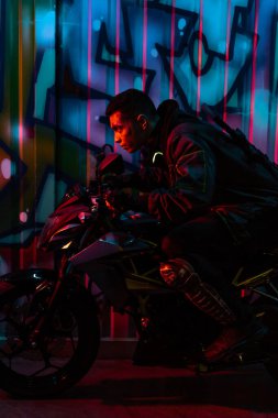 Sokakta üzerinde grafiti olan motosikletli karışık ırk siber punk oyuncusunun yan görüntüsü