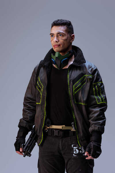 handsome and armed bi-racial cyberpunk player standing on grey  
