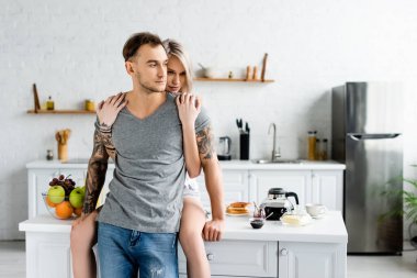 Beautiful woman embracing tattooed boyfriend near breakfast on kitchen table  clipart