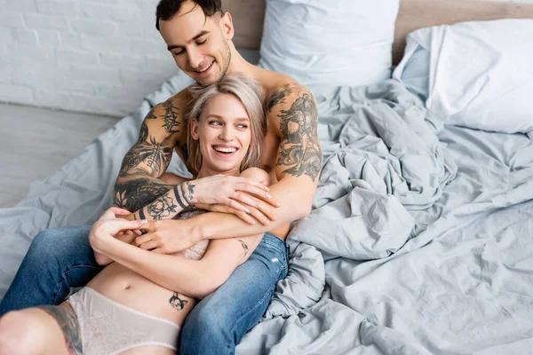 Bello Tatuato Uomo Abbracciare Sorridente Fidanzata Lingerie Sul Letto — Foto Stock