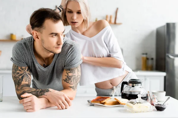 Vacker Kvinna Tittar Stilig Tatuerad Pojkvän Nära Frukost Köksbord — Stockfoto