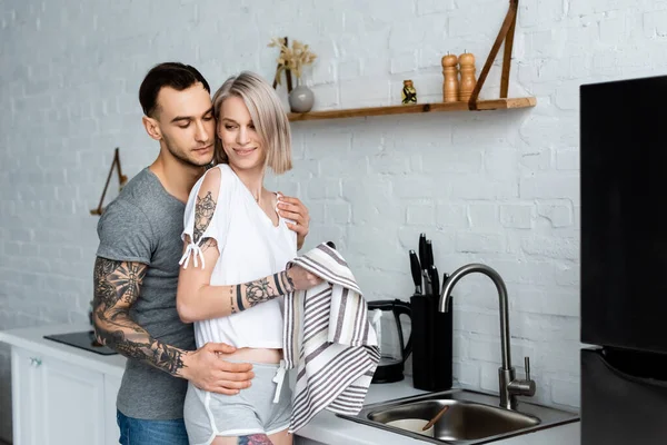 Boční Pohled Tetovaného Muže Objímající Krásnou Přítelkyni Ručníkem Kuchyni — Stock fotografie
