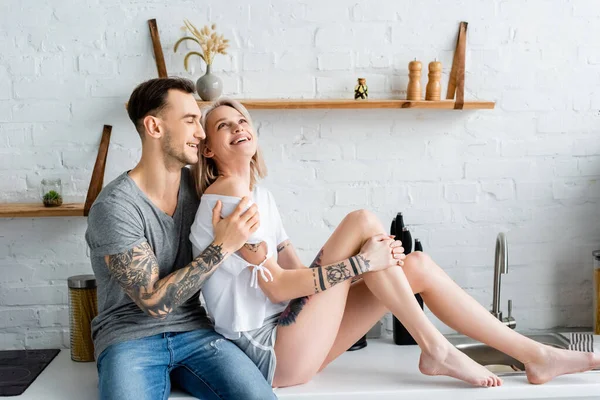 Lächelndes Tätowiertes Paar Umarmt Sich Auf Arbeitsplatte Küche — Stockfoto