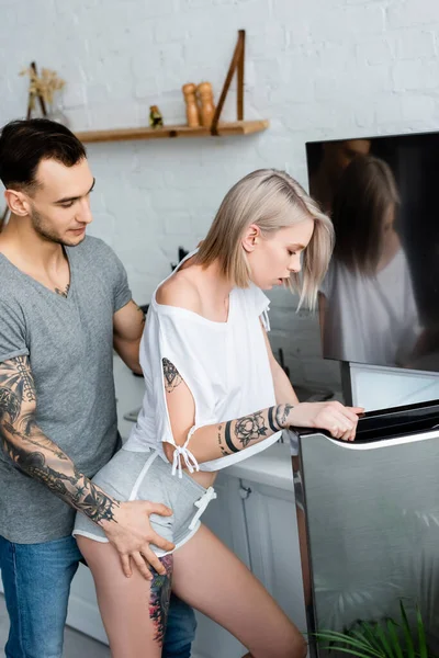 Вид Сбоку Красивого Мужчину Трогающего Чувственную Татуированную Подружку Возле Холодильника — стоковое фото