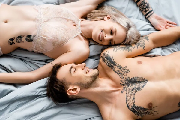 赤身裸体的男人在床上对着纹身的女友笑的照片 — 图库照片