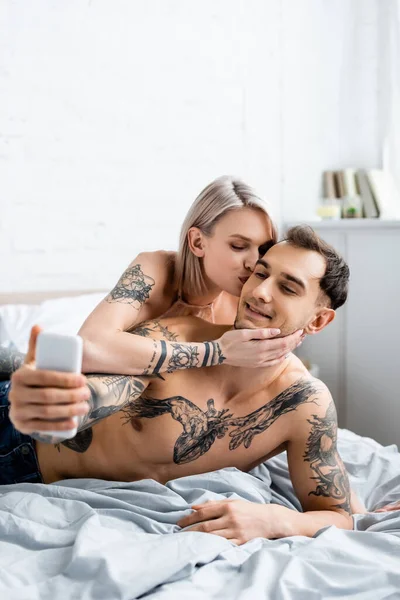 Vacker Flicka Kysser Skjorta Tatuerade Pojkvän Tar Selfie Med Smartphone — Stockfoto