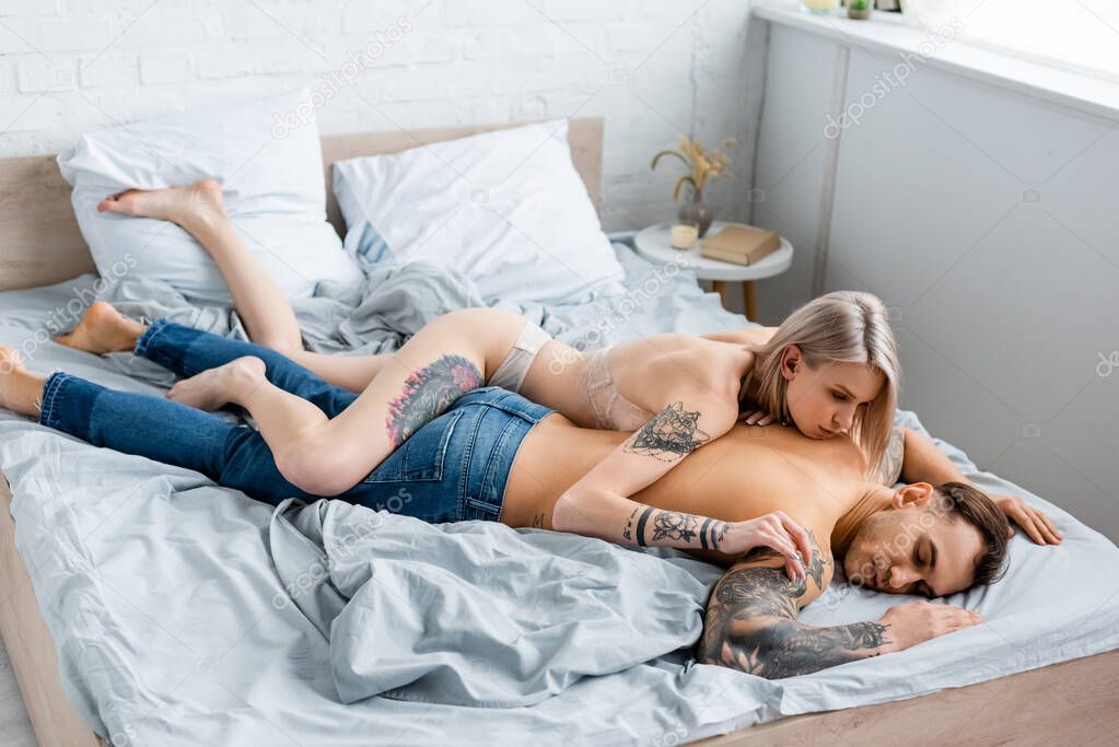 High angle view of beautiful woman in underwear lying on tattooed boyfriend on bed 