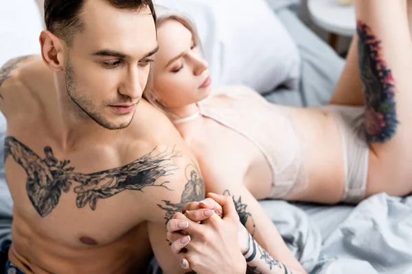 Foco Seletivo Homem Tatuado Segurando Mão Mulher Sensual Lingerie Cama — Fotografia de Stock