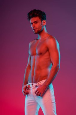 Seksi, kendine güvenen bir adam mor arka planda gradyan ile poz verirken kameraya bakıyor.