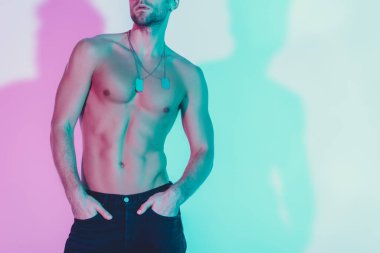 Koyu mavi kot pantolonlu, arka planda mavi ve mor gölgeli el ele tutuşan seksi gömleksiz bir adam.
