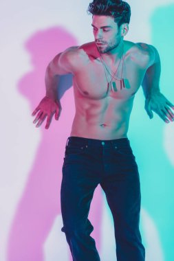 Koyu mavi kotlu seksi gömleksiz adam arka planda mavi ve mor gölgeli duvara yaslanıyor.