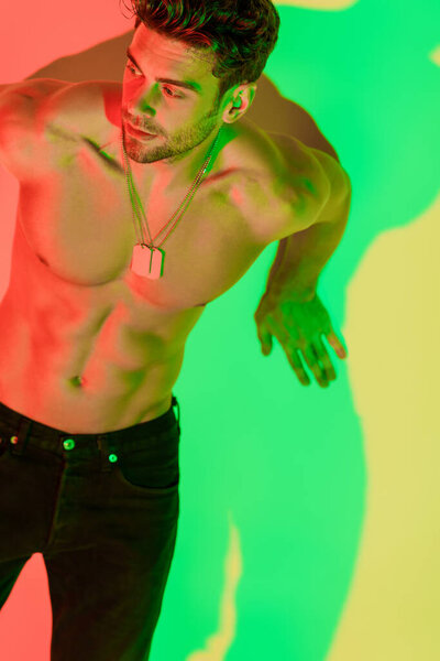 sexy, shirtless man leaning on wall and looking away on yellow with red and green shadows