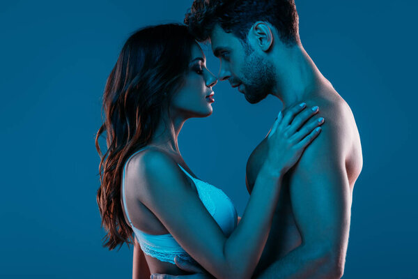 shirtless man and sexy girl in white bra hugging while standing face to face isolated on dark blue