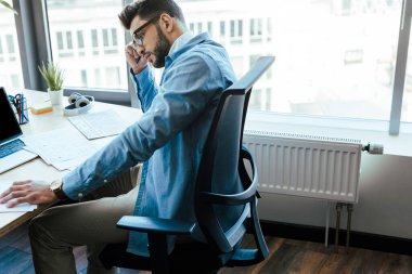 Thoughtful IT worker with documents at table in coworking space clipart