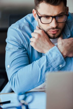 Kolları çaprazlanmış gözlüklü konsantre bilişim çalışanı seçici odağı