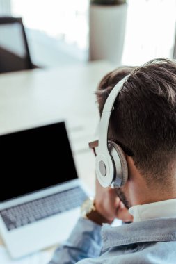 Kulaklıklı bilişim çalışanının seçici odak noktası laptopla birlikte çalışma alanı