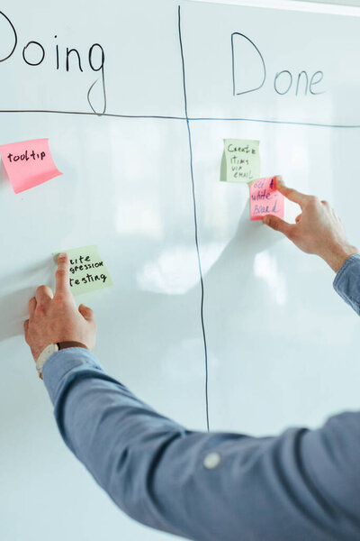 Cropped view of scrum master putting stickers on white board with spreadsheet with doing and done lettering