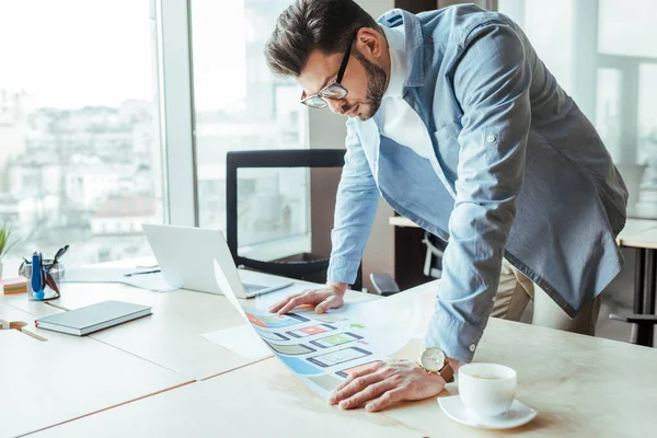 Konsentrert Designer Som Ser Vevd Papir Nær Kaffekopp Ved Bordet – stockfoto