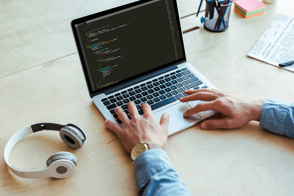 Partial view of developer working with laptop near headphones at table