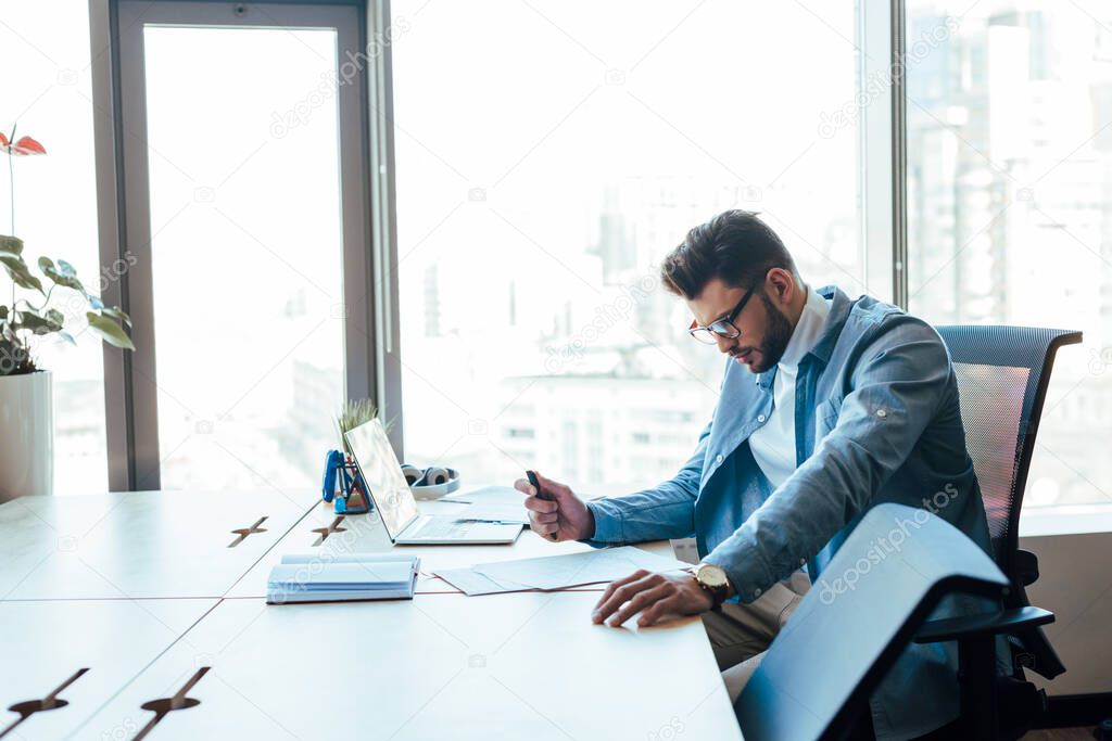 IT worker holding pen and looking at papers at table in coworking space