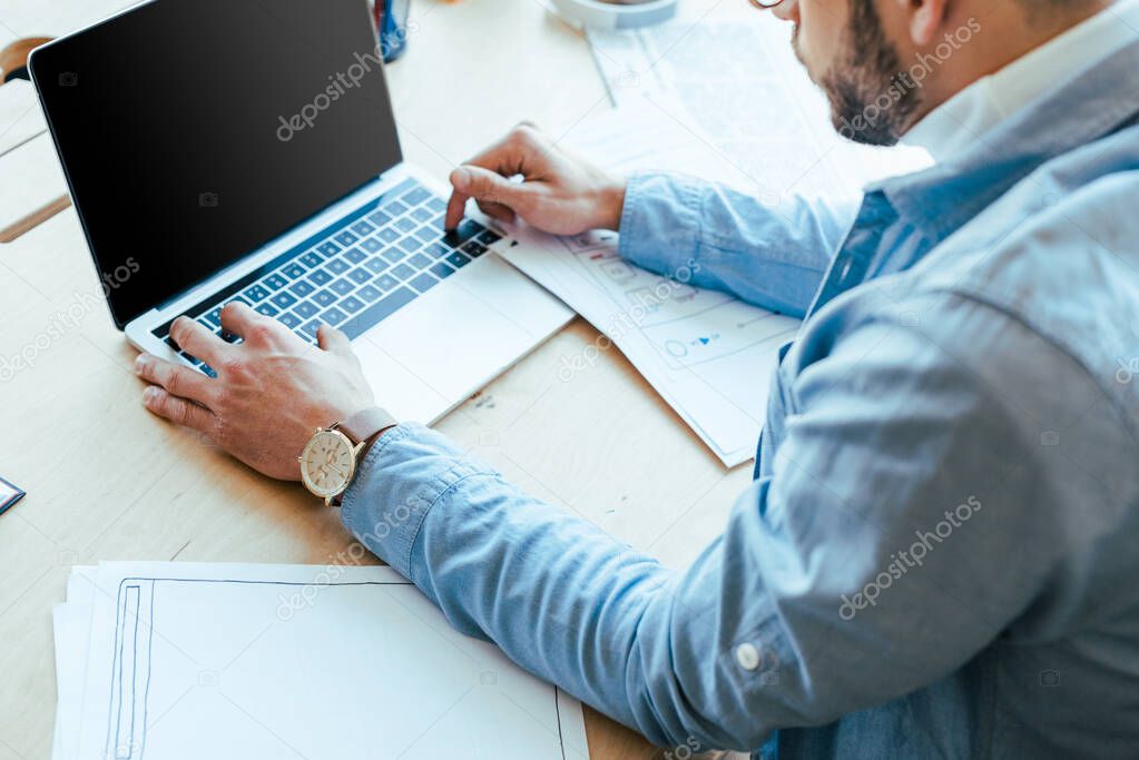 Cropped view of IT worker using laptop at table in coworking space