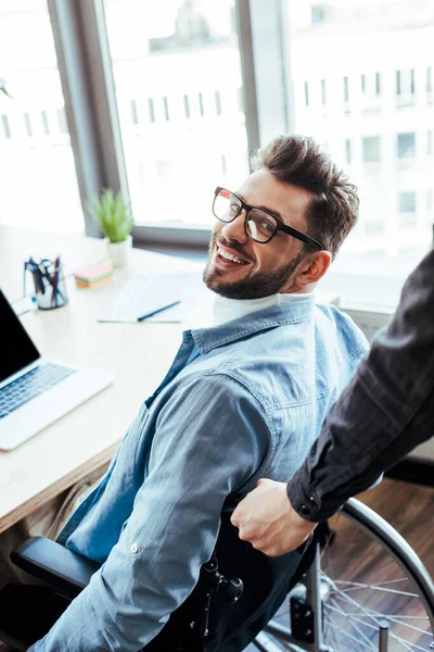 Disabled IT worker on wheelchair smiling and looking at camera at table in coworking space