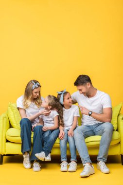 Mutlu ebeveynler sarı kanepede otururken tatlı kızlarıyla ve oğluyla konuşuyorlar.
