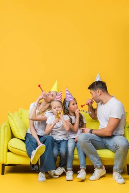 Mutlu ebeveynler ve çocuklar doğum günü partisi şapkaları ve sarı koltukta hava üfleyicileri. 