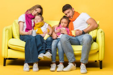 Sarı kanepede otururken gözleri kapalı nezle olan uykulu bir aile.  