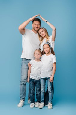 Mutlu ve çocuklu bir aile, mavi başlarının üstünde çatı jesti yapıyor.