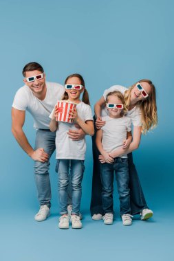 Neşeli bir aile 3 boyutlu gözlüklerle film izliyor ve elinde patlamış mısır kovası tutuyor.