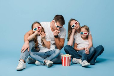 Üç boyutlu gözlüklü kafası karışık bir aile film izliyor ve elinde patlamış mısır kovası tutuyor.