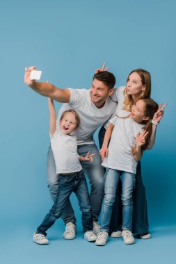 Neşeli aile zafer işaretleri gösterirken mavi telefondan selfie çekiyor.