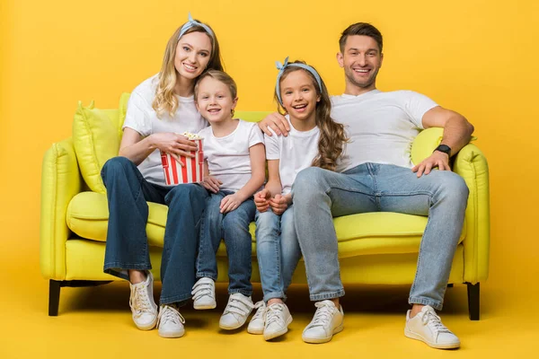 両親と子供たちは黄色のポップコーンバケツでソファで映画を見て笑っています — ストック写真