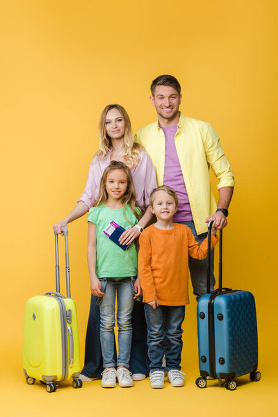 smiling family of travelers with luggage, passports and tickets on yellow