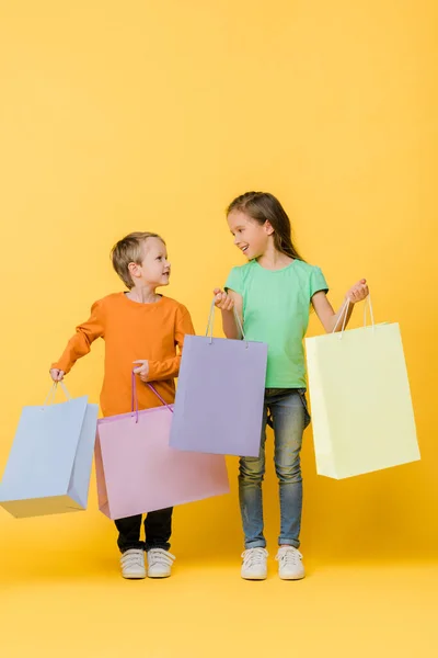 Niños Felices Sosteniendo Bolsas Compras Mirándose Uno Otro Amarillo — Foto de Stock