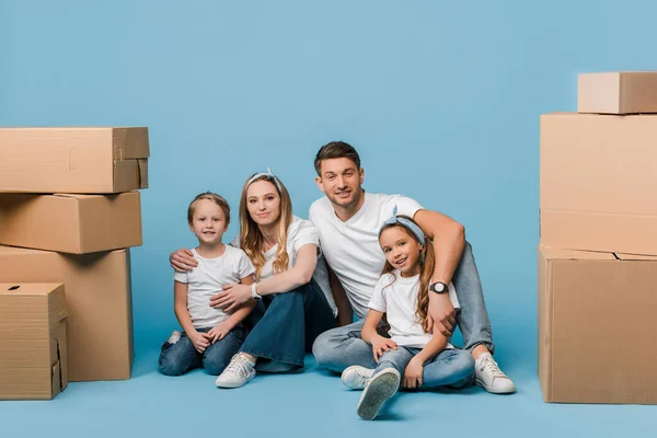 Happy Parents Hugging Kids Sitting Blue Cardboard Boxes Relocation — Stock Photo, Image