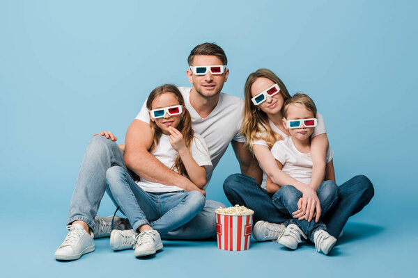 Счастливая семья смотрит фильм в 3D-очках с кукурузным батончиком на голубом
