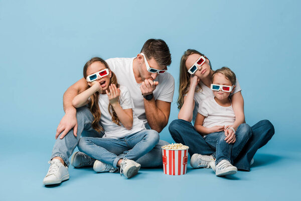 confused family in 3d glasses watching movie and holding popcorn bucket on blue