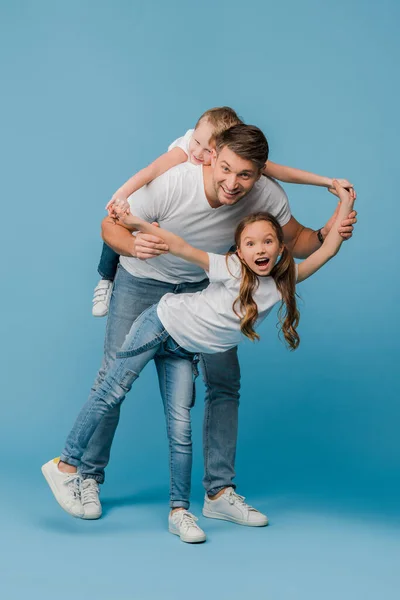 Sorrindo Pai Piggybacking Chapeamento Com Crianças Azul — Fotografia de Stock