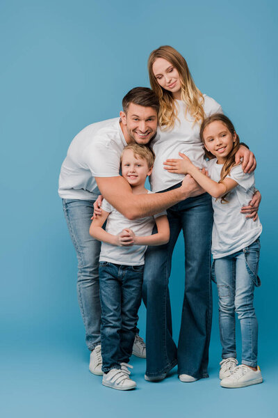 happy husband and kids hugging pregnant wife on blue 