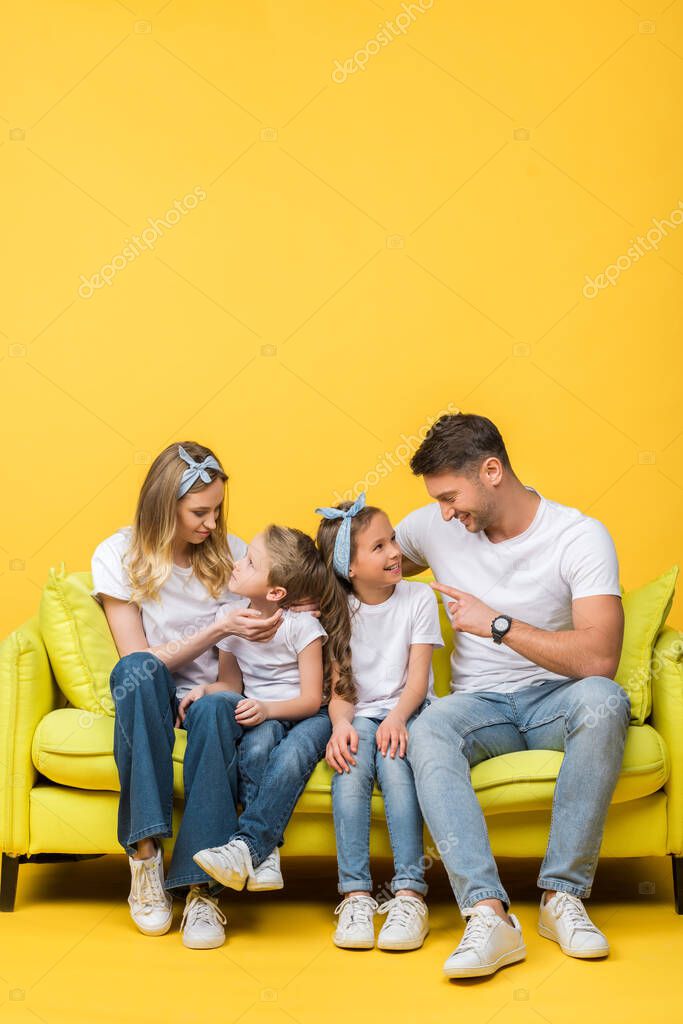 Happy parents talking with adorable daughter and son while sitting together on sofa on yellow