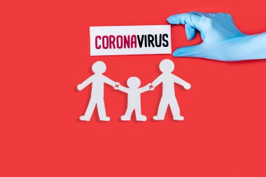 Doktorun üst görünümü lateks eldivenli elinde Coronavirus harfleri olan kırmızı üzerine izole edilmiş kağıttan insanlar. 