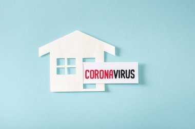 Mavi harflerle yazılmış Coronavirus yakınlarındaki kağıt evin üst görüntüsü.  