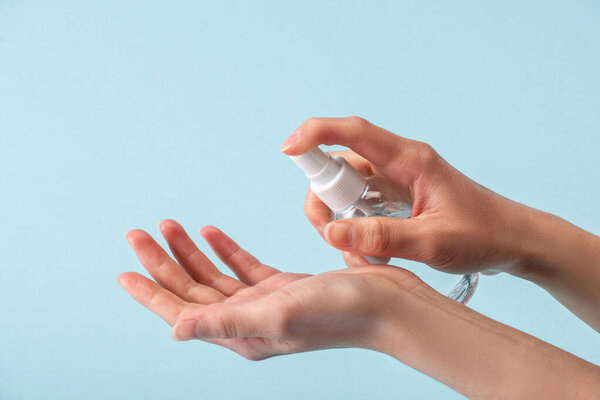 cropped view of woman holding spray bottle with hand sanitizer isolated on blue 