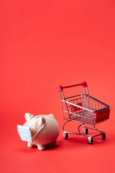 Sparschwein Kleiner Medizinischer Maske Neben Spielzeug Einkaufswagen Auf Rot — Stockfoto