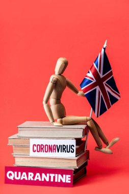 Birleşik krallığın bayrağını taşıyan tahta bebek karantina ve kırmızı harfli Coronavirus kitaplarının yanındaki kitaplarda. 