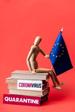 Karantina ve kırmızı harflerle Coronavirus yazılı kağıtların üzerinde Avrupa Birliği bayrağı olan tahta bebek. 