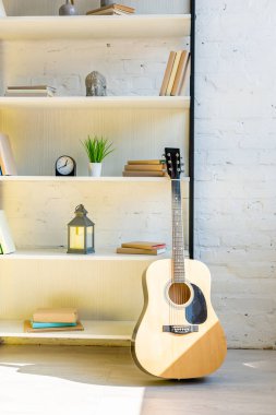 Akustik gitar kitapların yanında ve güneş ışığında saat.