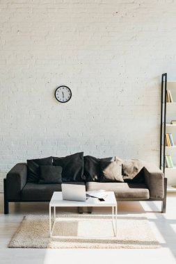 living room with grey sofa, shelf and table with laptop in sunlight clipart